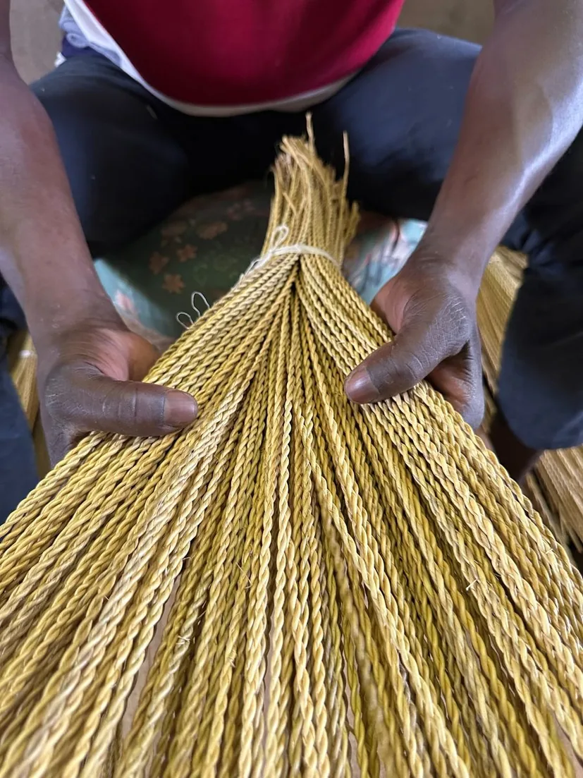 Hands rolling prepared strands of straw together on a wooden bench