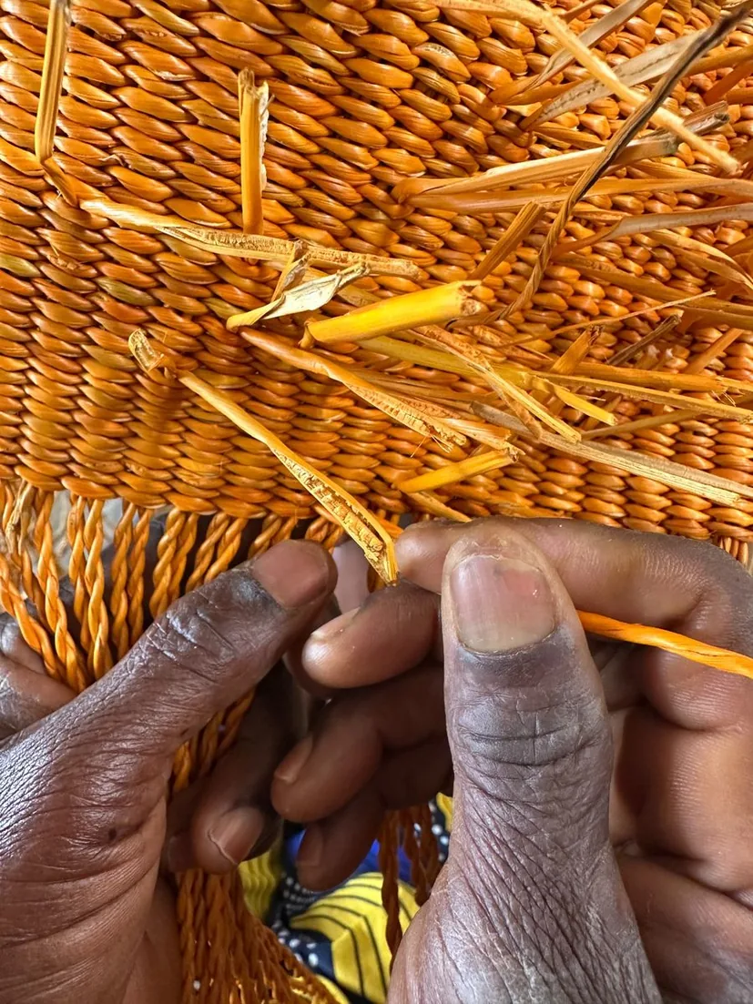 Close view of a hand weaving the golden straw basket structure
