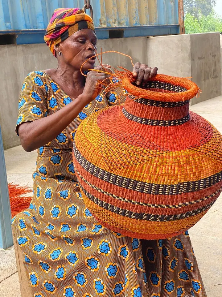 A basket maker finishing a round basket with orange and green bands